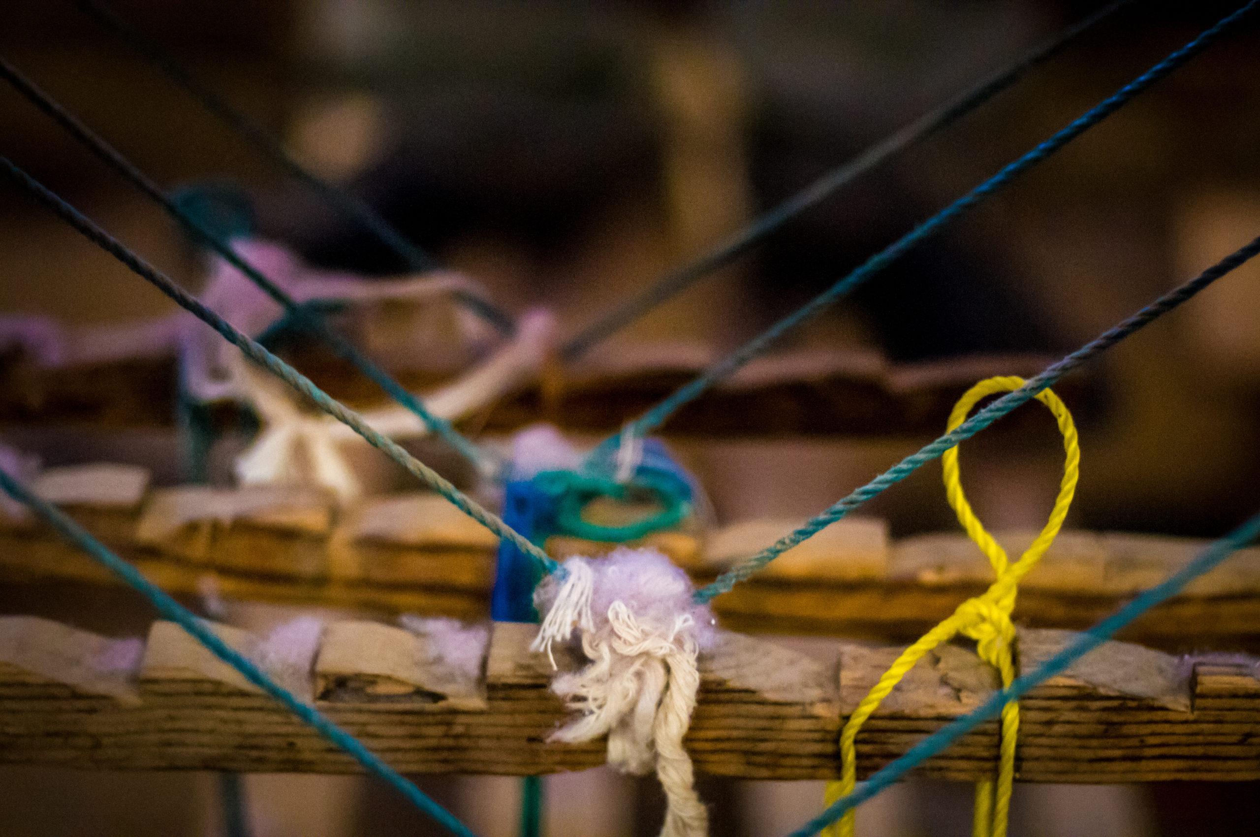 Mechones de lana y cordeles de colores anudados sobre una viga de madera en un taller de Teotitlán del Valle
