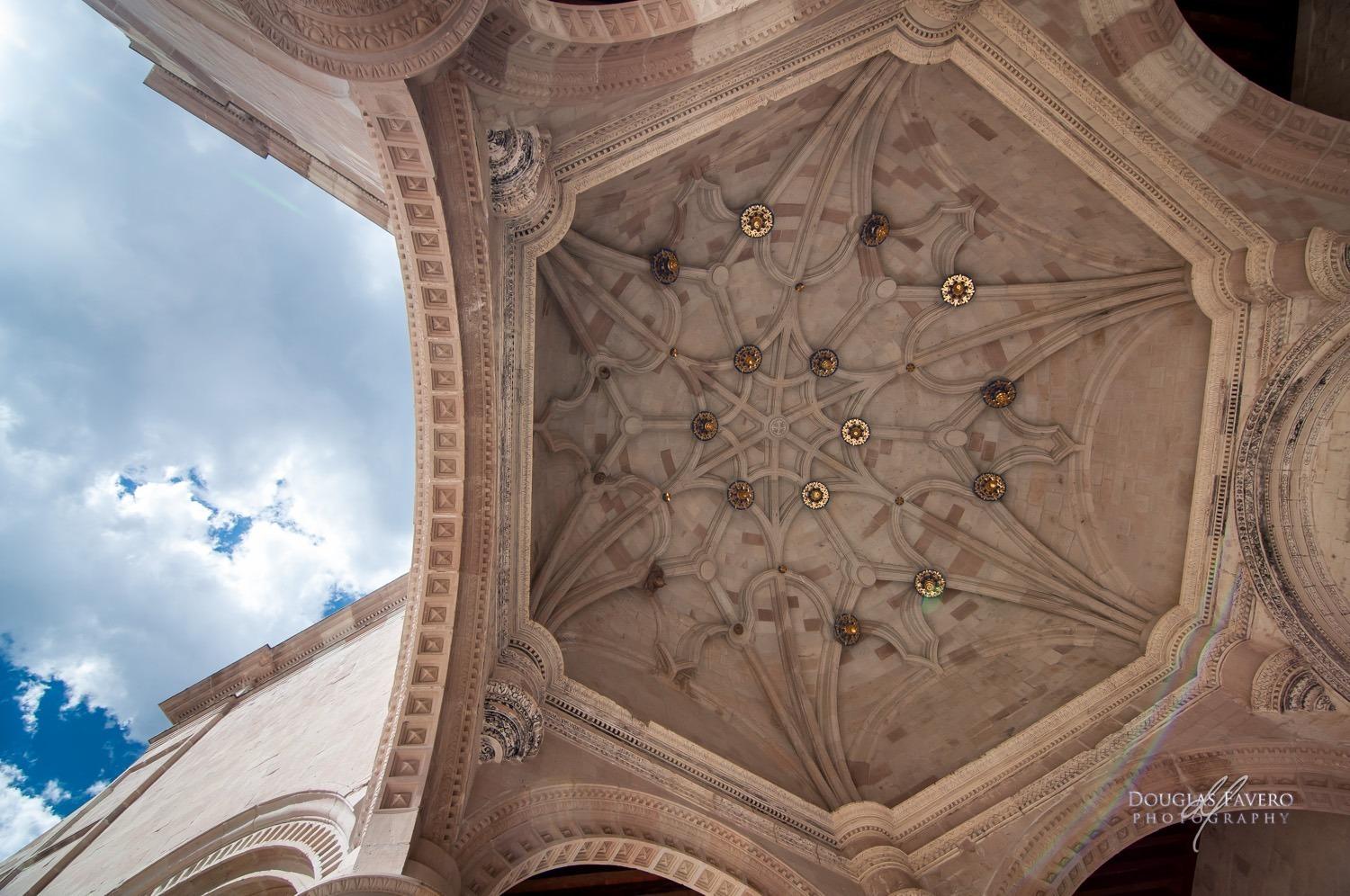 Bóveda nervada de la capilla abierta de Teposcolula vista desde abajo, con florones dorados y cielo azul
